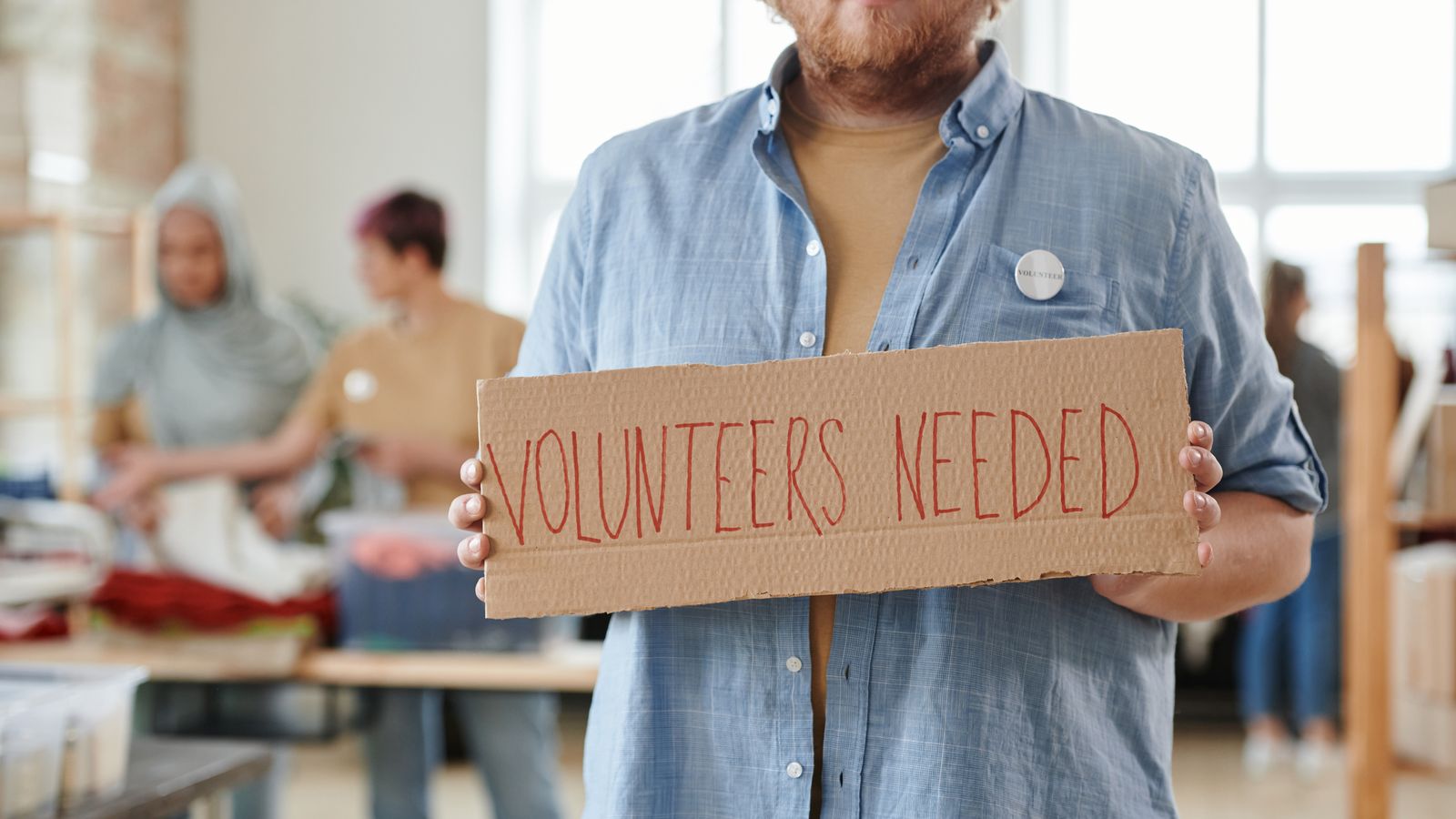 Volunteer holding a hand painted volunteers needed sign at a community drive